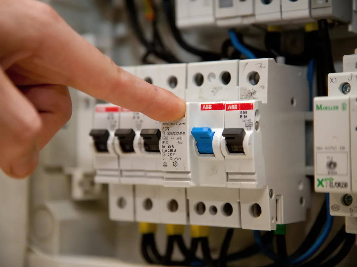 Finger am FI-Schutzschalter im geöffneten Sicherungskasten